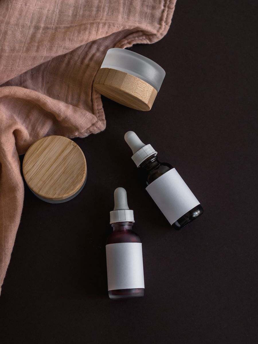 A dropper serum bottle and a bamboo-lidded jar on a dark surface.