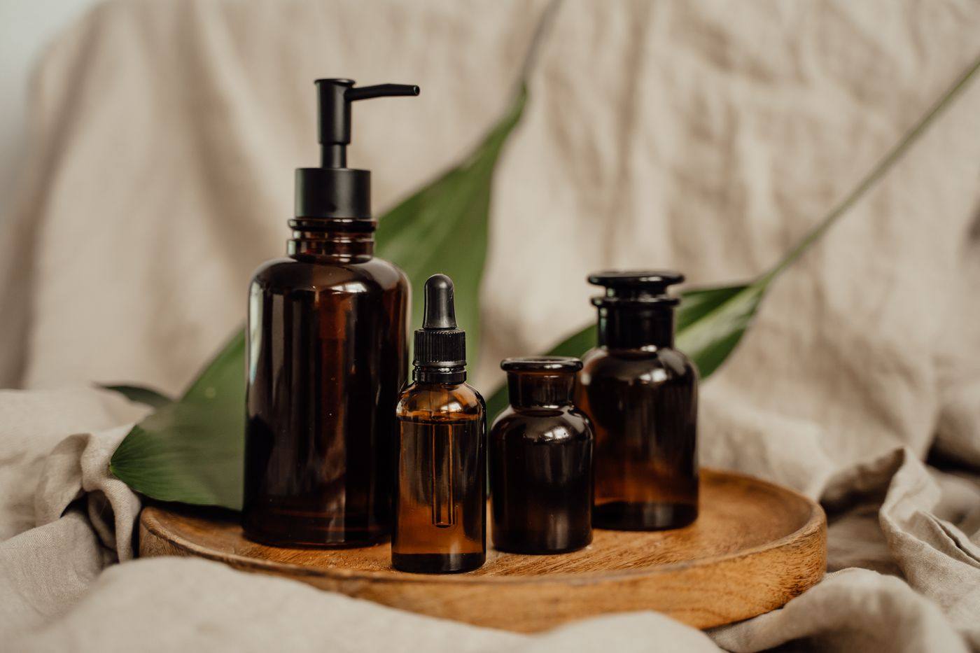 Amber apothecary bottles and a dropper serum on a wooden tray, styled with linen and a leaf.
