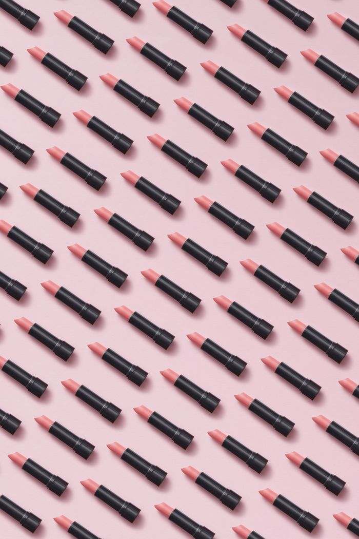 A repeating pattern of coral lipsticks on a pink background.